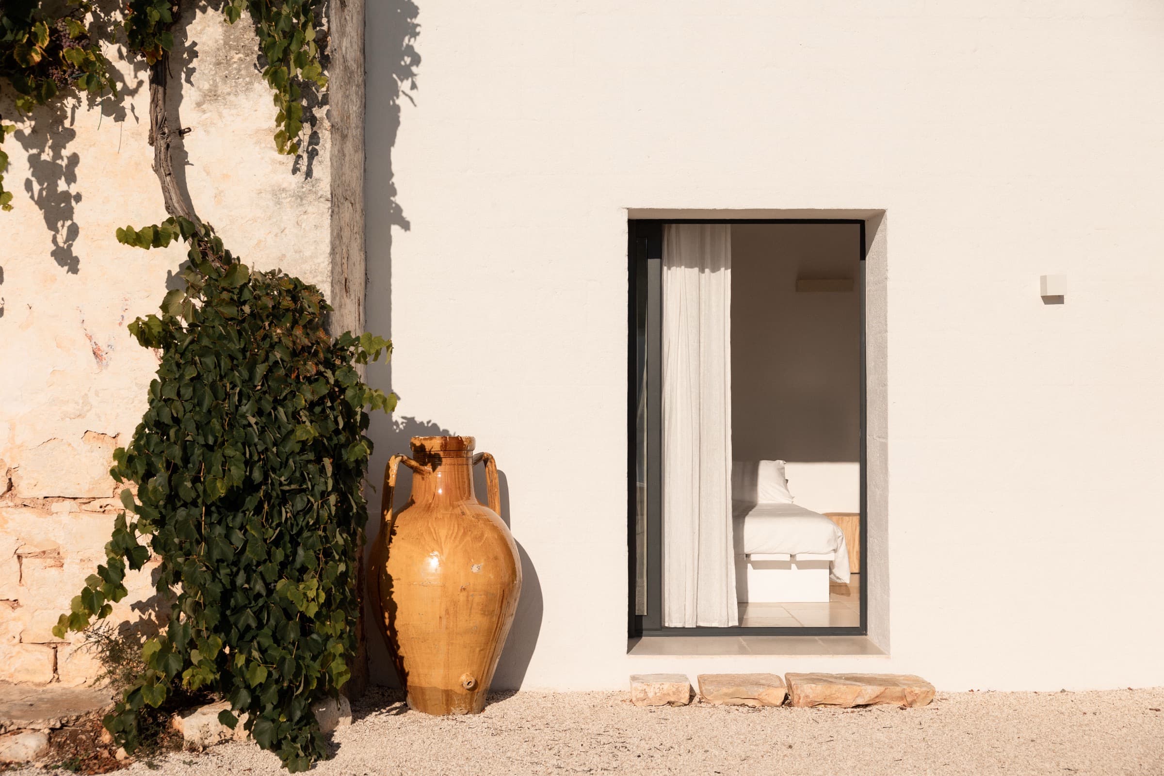 A whitewashed masseria wall with a terracotta amphora and a curtained doorway, near Ostuni